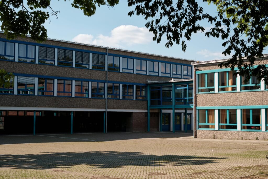 Exterior view of a modern educational building in Geilenkirchen, Germany, featuring large windows and a paved courtyard.
